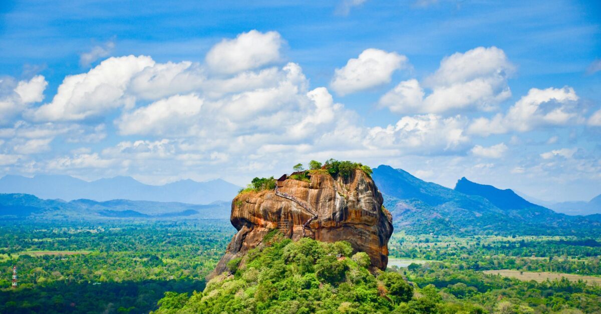 Explore the iconic Sigiriya Lion Rock surrounded by lush greenery and vibrant blue skies in Sri Lanka.
