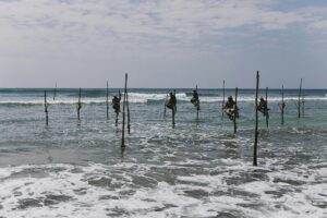 Stilt fishermen perched over ocean waves in Sri Lanka, showcasing a timeless cultural tradition.