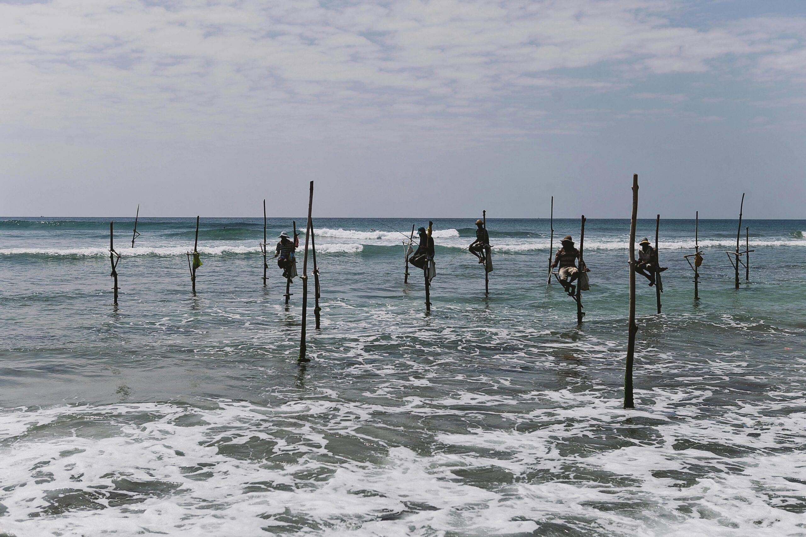 Stilt fishermen perched over ocean waves in Sri Lanka, showcasing a timeless cultural tradition.