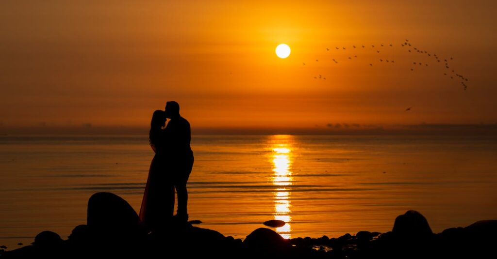 A couple silhouettes embrace during a stunning ocean sunrise.