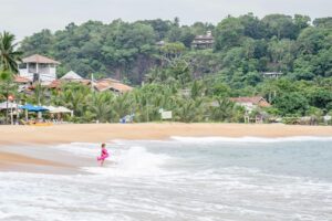 A child plays in the ocean waves at a serene tropical beach in Sri Lanka.